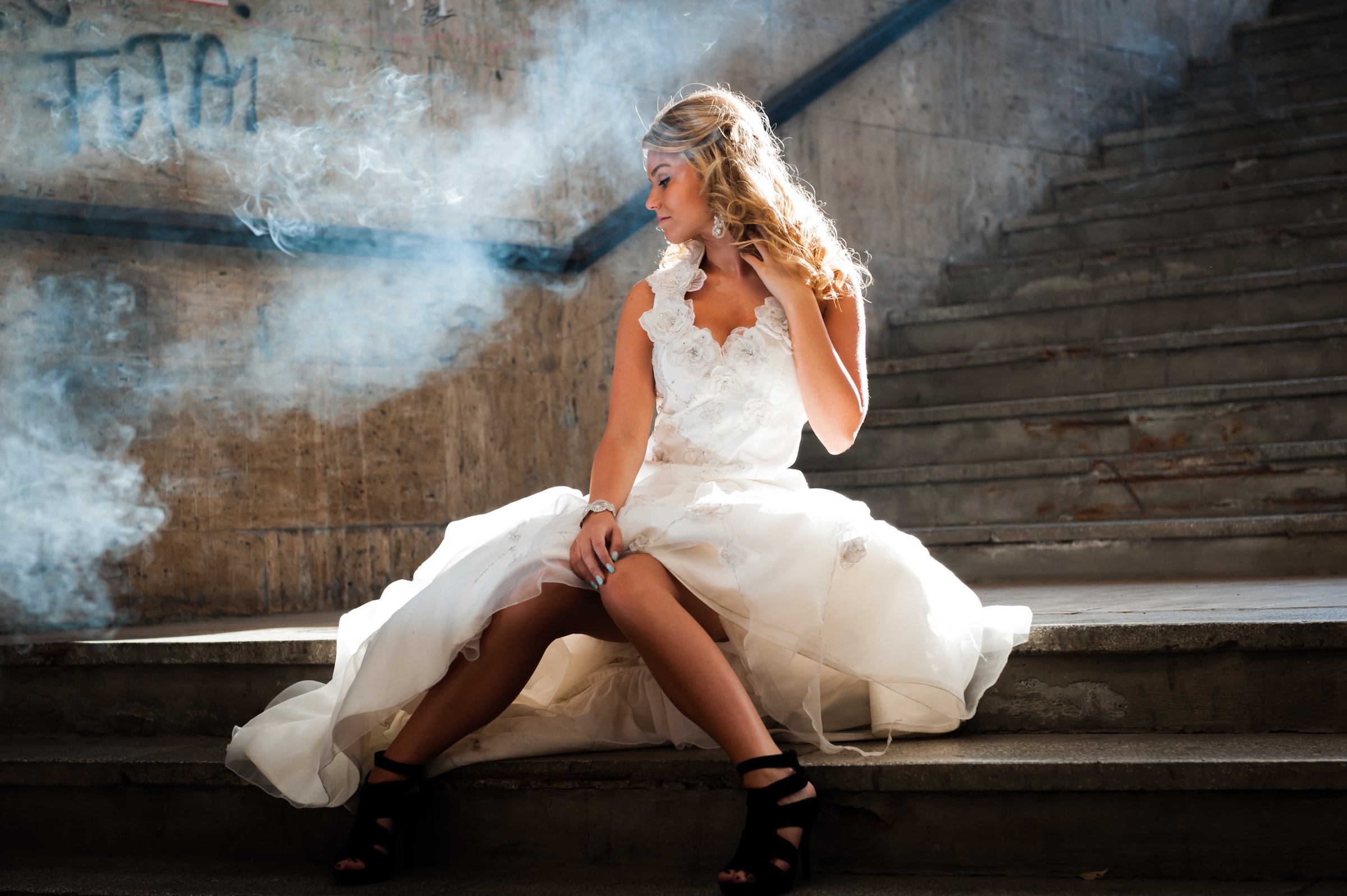 bride with wedding dress sitting on stairs with white smoke in the background