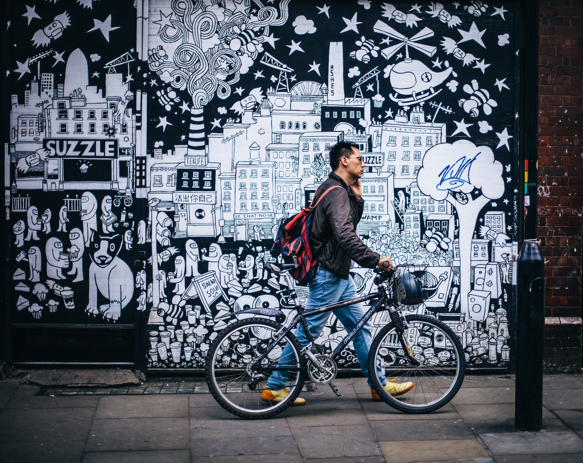 man in black jacket holding a black hardtail bike near black and white art wall