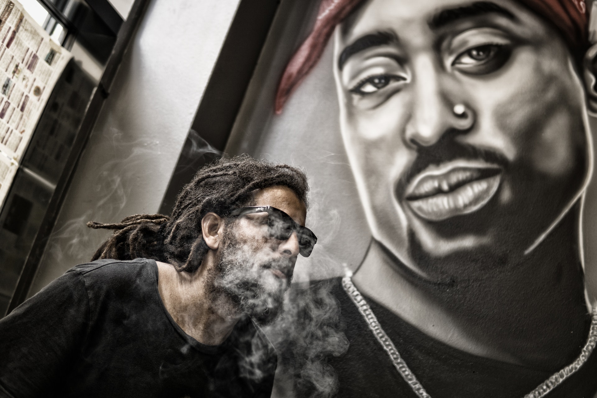 man with dreadlocks and sunglasses poses near Tupac shaker portrait