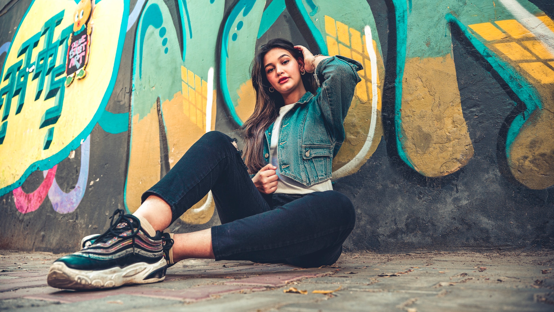 a woman sitting on the ground against a wall with graffiti